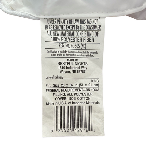 A close-up image of a care label attached to a Restful Nights Ultra Essence Pillow | Medium Firmness, stating it's made from 100% antimicrobial fiber fill, with care, legal, and material information including barcode, made in the