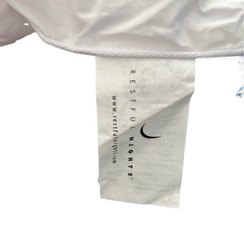 A close-up of a white clothing tag with black text and a Nike logo at the bottom. The text reads "Restful Nights Ultra Essence Pillow | Medium Firmness" with additional web and email contacts below. The tag is attached.