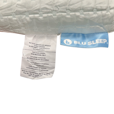 A close-up image of a Blu Sleep Bio Aloe Vera pillow with a part of its tag visible. The tag features washing instructions and manufacturer details, including the brand name "blu sleep." The pillow is white.