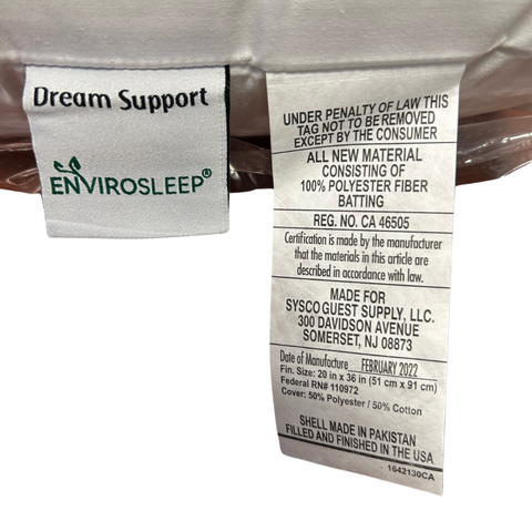 Two clothing labels on a transparent plastic-wrapped Manchester Mills Envirosleep Dream Support Pillow. The top label says "Envirosleep Dream Support," and the lower label includes care instructions, material details (50% cotton...