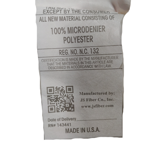 A crumpled clothing tag displays text indicating material composition as "100% microdenier polyester," a QR code, the manufacturer "JS Fiber Co., Inc.," and a statement "Made in Keeco.