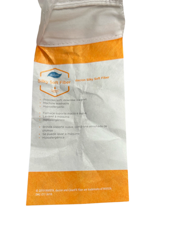 A crumpled tag showing details of the JS Fiber® Invista Comforel® Gussetted Pillow, made from silky soft fiber material with properties such as machine washable, hypoallergenic.