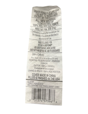A close-up of a Carpenter Co. Dual Layered Comfort Pillow's care label, detailing material composition of the cover and filling, care instructions, and identification numbers, indicating it is made with 100% polyester.