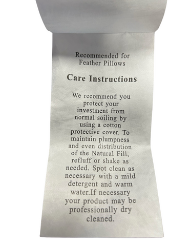 Close-up of a care instruction label for Encompass Group 50/50 Gray Duck Feather and Down Pillows, advising on regular cleaning with a cotton cover, maintaining shape, spot cleaning, and suggesting a dry cleaner for stubborn stains.