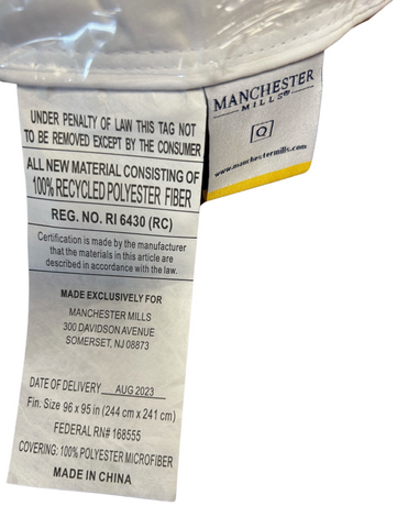 A close-up of a white textile label from Manchester Mills on an Envirosleep® Tempo Polyester Duvet Insert | Summer Weight, detailing product information including material composition, size, and regulatory compliance, emphasizing its environmentally friendly features.