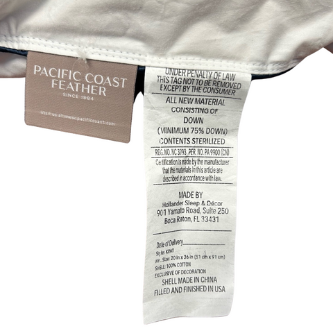 A close-up of a Pacific Coast Feather Company Grand Embrace<sup>®</sup> Pillow's care label attached to its seam. The label shows instructions and material content details, including 75% down and 25% other materials, with additional organic cotton cover details.
