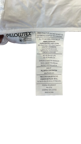 Close-up of a care label attached to a white Pillowtex Triple Core White Duck Down & Feather Pillow labeled "Pillowtex." The tag provides material content details and care instructions, including warnings.