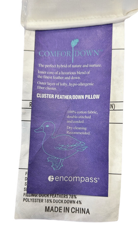 A label for a Pillow Factory Comfort Down Pillow, describing the hybrid of nature and comfort. It features a duck outline on a shopping cart, specifying 100% cotton, allergy-tested, with