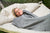 A woman relaxes outdoors on a cushioned hammock, wrapped up to her shoulders in the American Blossom Linens Wool Throw Blanket—Made in USA with soft, natural climate-beneficial wool and a gray-and-white chevron weave.