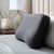 A Malouf HexCurve™ Pillow with a hexagon pattern stands upright on a neatly made bed with light gray bedding. Behind it, a wooden nightstand displays a marbled vase, a white ceramic vase with branches, and a lamp with a white shade.