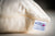 A close-up of the American Blossom Linens Wool Filled Pillow—Organic Cotton, Adjustable Firmness—shows a cream cover with zipper and a white label reading “American Blossom Linens, 100% U.S.A. organic cotton” alongside a small pink flower graphic.