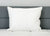The Down Etc. Fairfax Pillow - Featured at St. Julien Hotel & Spa® is a large, white, square down alternative pillow with firm support, ideal for side and back sleepers, shown upright on a light gray tufted sofa against a matching wall.