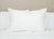 A single Pillowtex Premium Polyester Pillow | Firm stands on a white quilted bed against a beige wall. The smooth, firm polyester pillow by Pillowtex contrasts with the textured bedding and neutral backdrop.