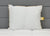 The JS Fiber Super Gold Choice Pillow | Heavyweight by JS Fiber, featuring a white square design with gold trim and yellow tag, sits upright on a tufted mattress against a gray headboard—ideal support for side sleepers.