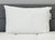 A large, fluffy white Envirosleep Dream Support Pillow by Manchester Mills, featuring two visible tags, is propped against a gray headboard on a white quilted mattress, creating a clean and comfortable setting focused on support.