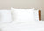 A neatly made bed with a wooden headboard features a white comforter and three upright Pillowtex Premium Polyester Pillows | Firm against a light beige wall, creating a clean, minimal, and comfortable scene—ideal for side sleepers.