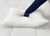 A person in dark blue pajamas presses a hand into a Pillow Factory Comforel Pillow, featured at Sheraton Hotels, on a white quilted mattress, showcasing its plush, hypoallergenic softness as it visibly compresses.