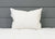 A Pillowtex White Duck Down & Feather Pillow (95% feathers/5% down) with small side tags rests upright against a gray upholstered headboard on a neatly made, white quilted bed, creating a clean and minimalistic scene.
