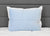 A Pillowtex Cooling Gel Pillow Protector rests against a white pillow on a white quilted bed. The headboard is upholstered in gray fabric with horizontal seams, creating a clean and tidy look.