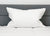 A Down Etc. 50% White Goose Down / 50% White Goose Feather Pillow rests against a gray upholstered headboard on a white quilted bed, creating a clean and minimal look with soft lighting and no extra decor.