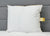 The JS Fiber Super Gold Choice Pillow | Heavyweight by JS Fiber, featuring gold trim and label, sits against a gray padded headboard on a white quilted bed. Filled with siliconized fiberfill, it's plush and ideal for side sleepers seeking comfort.