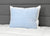 A white pillow with a Pillowtex Cooling Gel Pillow Protector in a light blue grid pattern rests against a gray headboard on a white quilt, creating a clean, modern look and showcasing the comfort and coolness of Pillowtex.