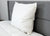 The Down Etc. Fairfax Pillow—featured at St. Julien Hotel & Spa®—stands upright against a gray upholstered headboard on a white comforter, offering plush comfort and firm support for side and back sleepers.