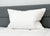 The Down Etc. 50% White Goose Down / 50% White Goose Feather Pillow rests upright against a dark gray headboard on a neatly made white, quilted mattress, creating a clean and inviting modern sleeping environment.