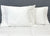 Two white pillows with Pillowtex Cotton Pillowcase Set (2 pillowcases) rest against a gray upholstered headboard on a neatly made white quilted bed, creating a clean, minimal look.