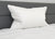 The Down Etc. 50% White Goose Down / 50% White Goose Feather Pillow from Down Etc. with medium support stands upright against a gray headboard on a neatly made bed, creating a clean, minimal scene of comfort and relaxation.