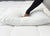 A hand in a long black sleeve presses down on the Manchester Mills Envirosleep Dream Support Pillow, set on a white quilted mattress, showcasing the pillow’s plush and hypoallergenic texture.