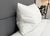 A Down Etc. 50% White Goose Down / 50% White Goose Feather Pillow rests against a gray upholstered headboard on a neatly made bed with a white comforter, while a potted plant and black tripod lamp add charm to the modern bedroom.