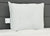 A square white JS Fiber Hollofil II Pillow | Medium with a visible tag sits upright against a dark gray cushioned headboard on white quilted bedding. The well-lit scene highlights the JS Fiber pillow's clean, smooth, and hypoallergenic surface.
