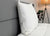 The Down Etc. Fairfax Pillow—featured at St. Julien Hotel & Spa<sup>®</sup>—rests upright against a grey headboard on a tidy bed, with a potted plant and floor lamp nearby for a serene scene perfect for side and back sleepers.