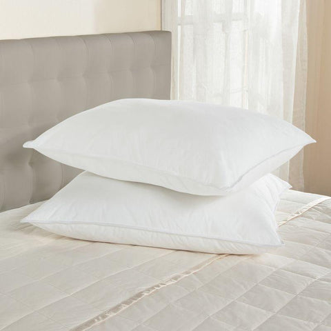 Two plush Downlite® White Goose Feather Pillows in Medium Support rest atop a neatly made bed with a taupe quilt, evoking a serene and comfortable atmosphere in a room filled with soft, natural light.