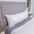 The Pillowtex Premium Polyester Body Pillow (Medium Support) by Pillowtex is displayed on a gray sheet atop a neatly made bed with a light gray fabric headboard, flanked by white nightstands and a window featuring pampas grass in a vase.