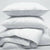 A stack of fluffy white JS Fiber Gold Choice Polyester Pillows against a grey background, suggesting softness and comfort with their hollow siliconized fiberfill for a peaceful sleep environment in hotel franchise properties.