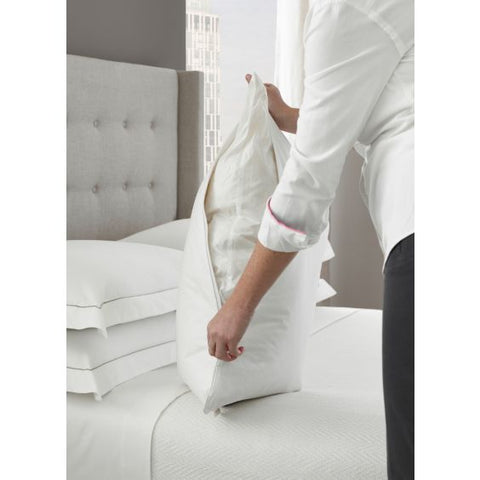 A woman placing a Manchester Mills Temperloft ReNew Pillow Down/Down Alt Fill | Firm Support on a bed, making it environmentally friendly with its recycled polyester fibers.
