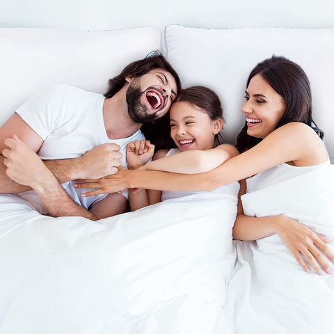 Happy family laughing in bed with JS Fiber Invista Comforel Gussetted Pillows at home stock photo.