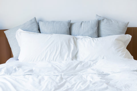 A bed with white sheets and an Encompass Group Gray Goose Feather and Down Pillow for added comfort.