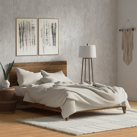 A serene bedroom featuring a modern wooden bed with a Delilah Home Organic Cotton Duvet Cover, a white rug, minimalist artwork, and a macramé wall hanging, complemented by a simple side lamp and fresh plant.