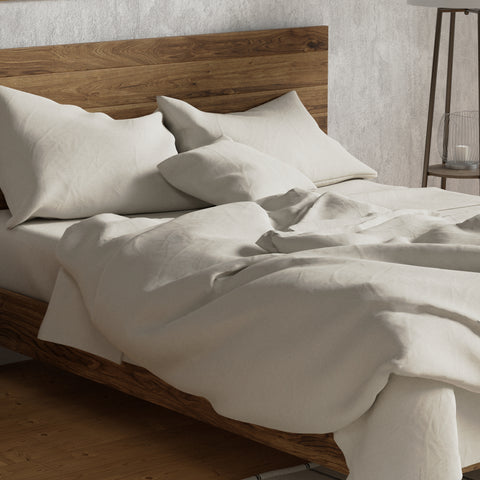 A neatly made bed with a wooden headboard, cream-colored Delilah Home Organic Cotton Duvet Cover and plush pillows, set in a room with a soothing, minimalist aesthetic and hardwood flooring.