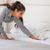 A woman is cleaning a hotel bed with a Down Etc. Rhapsody Wrap Down/Feather Pillow- Featured at Many Hyatt® Hotels.