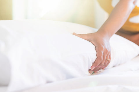 A woman is placing a Down Dreams ReNew Soft Pillow by Manchester Mills on the bed.