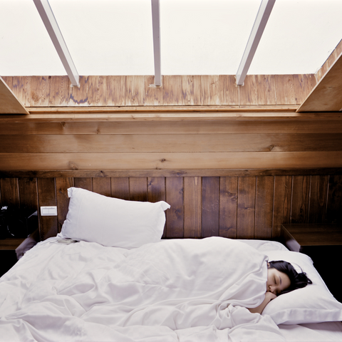 A woman peacefully sleeping on a bed using a Envirosleep Platinum Garneted Polyester Fiber Fill Pillow from Manchester Mills.