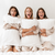 Three women in white robes sitting on a bed with Hollander Holiday Inn® Soft Support Pillow Combo Pack | Polyester and Down & Feather (Includes 2 Pillows), providing each other support.