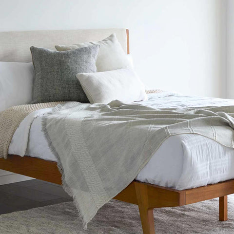A bed with a Fairkind La Marea Alpaca Throw Blanket in white and grey.