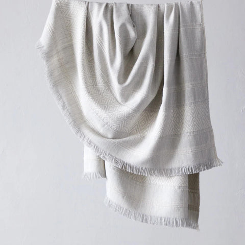 A soft Fairkind La Marea Alpaca Throw drapes elegantly on the white wall.