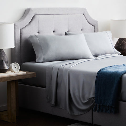 A bed with eco-friendly Malouf Tencel Sheet Set and a lamp on the side.