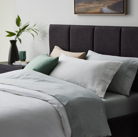 A bed with Malouf Linen-Weave Cotton Sheet Set sheets and a green plant on it.